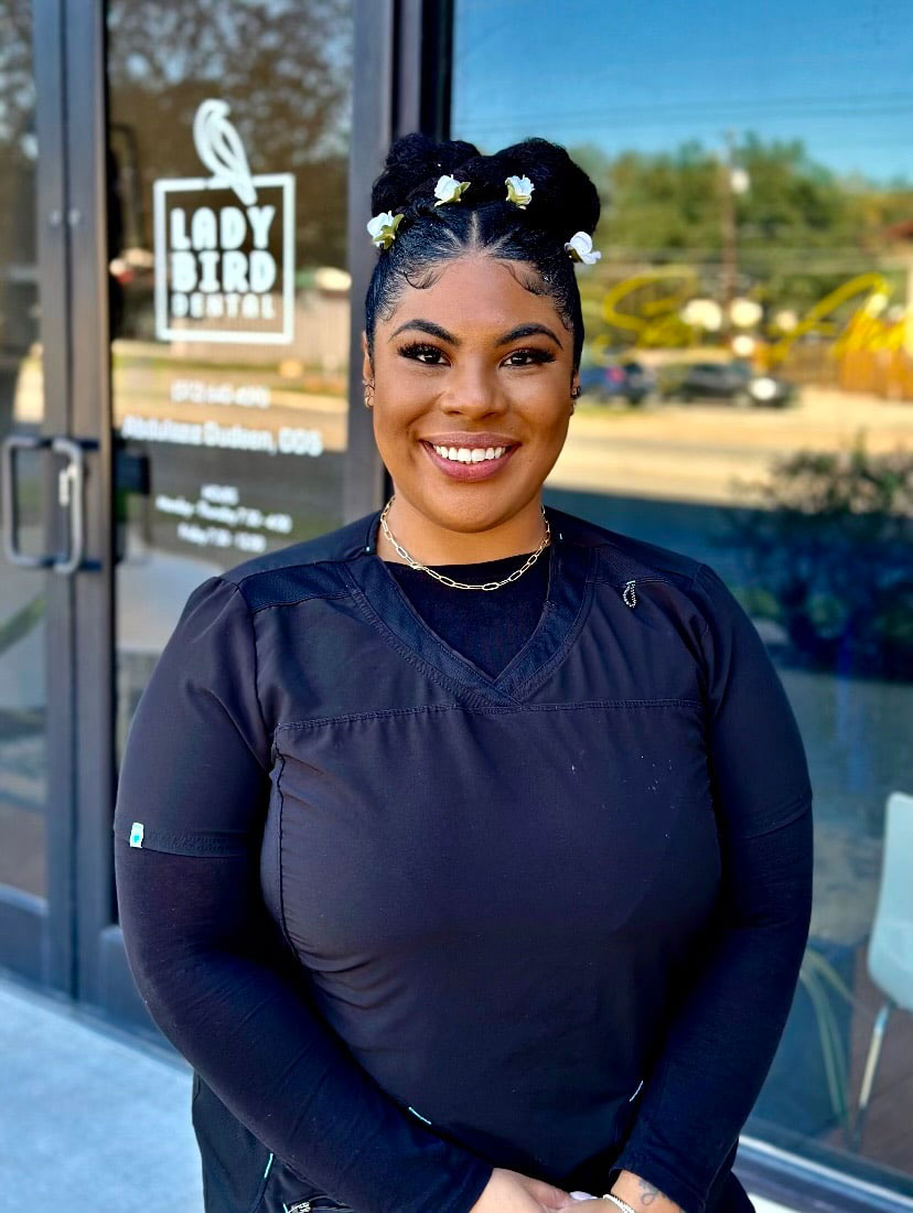 A woman wearing a black shirt and a hair accessory stands smiling in front of a storefront with a bird logo, posing for the photo.